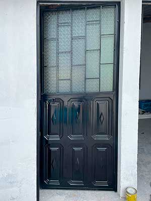 Puerta metálica con tool panelado y protección tipo ladrillo para entrada